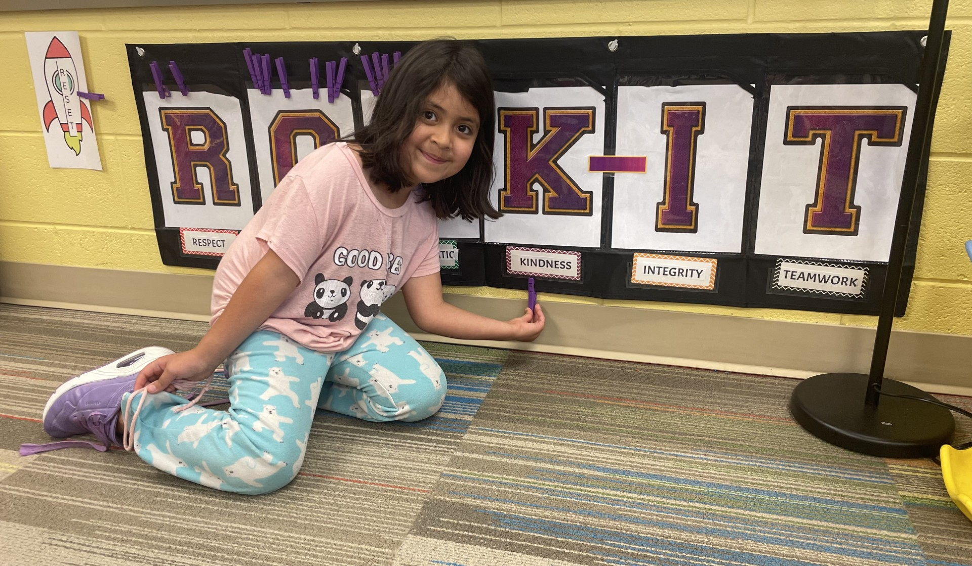 A child kneeling on the floor holding a purple markerDescription automatically generated